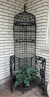 Front view of vintage wrought iron birdcage bar with glass table top and faux plant inside.