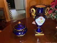 Photo featuring the blue cobalt lidded dish with lid and gold finial along with the deep blue vase with floral and gold detailing.