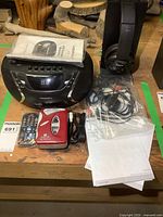 Front view of Nexxtech boombox, Audiovox radio, Sony headphones with cables and manuals on wooden surface