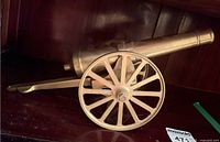 Photo of the brass model cannon from the side showing wooden spoked wheel and barrel details.