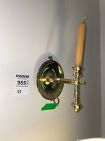Pair of brass candle holder wall sconces mounted on a wall, showing reflective circular brass backplate and candle arm with yellow taper candle.