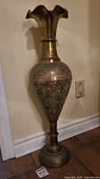 Full view of tall brass vase showing body with etched floral and circular geometric designs and flared neck.