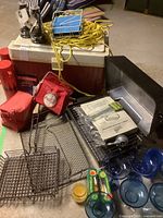 Photo showing vintage Thermos cooler, two red lunch bags, grilling racks, plastic margarita glasses, gas BBQ, and yellow rope.