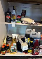 Shelf view showing various car cleaning and care products including polish, leak seal, degreaser spray, and microfiber towels with red trim.