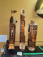 Front view of three carved wooden castle sculptures with detailed features and ladders, signed and dated 2020.