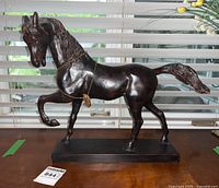 Front view of dark brown cast iron horse with raised front left leg on rectangular base