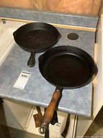Two 10-inch cast iron frying pans on countertop, one with a wooden handle, the other with cast iron handle. Both pans show surface wear.