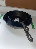 Two cast iron frying pans stacked, showing difference in size and handle design with pour spouts