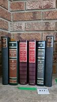 Front view showing six hardcover classic books arranged upright against a brick wall.
