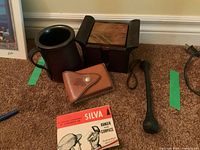 Wood coasters in rack, metal mug with leather cover, Silva compass with case and manual, and a billy club laid out on carpet