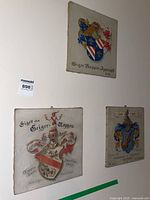 Three square canvas prints featuring coat of arms symbols on a white wall.