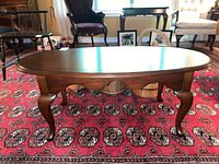 Full front-side view of the oval wooden coffee table showcasing polished surface, cabriole legs, and apron detail.
