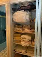 Closet shelves with folded linens including comforter covers, towels, and placemats.