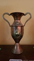Front view of the vase showing its two curved solid brass handles and brass decorative medallion on copper body.