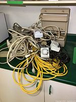 Lot of electrical extension cords tangled together with multiple mechanical timers placed on top, and beige plastic cabinet racks at the back.