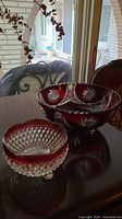 Photo showing two Bohemian crystal bowls with ruby red rims on a dark wooden table by a window.