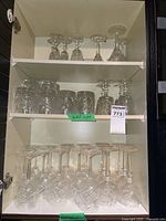Full cabinet shelf showing multiple sets of leaded crystal stemware and cocktail glasses with various etching styles.