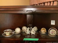 Two full size cups and saucers, four demi tasse cups and saucers, and two tiny creamers displayed on shelf.