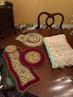 Full view of multiple vintage doilies and lace tablecloth on wooden dining table.