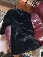 Black faux fur coat laid on red leather couch, showing full length and plush texture