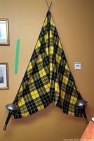 Two fencing foils crossed and draped with yellow and black MacLeod tartan fabric hanging on a wall for display.