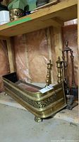 Photo of brass fireplace fender, brass andirons, and fireplace tool set in basement setting