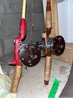 Photo showing two fishing rods with Penn Peer No. 209 reels and cork handles placed against concrete wall in garage.