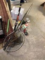 Overview of two rods leaning next to landing net and line spools on basement floor