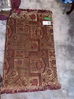 Full view of the brown, beige, and red patterned 3x2 floor mat with fringed edges lying on carpeted floor.