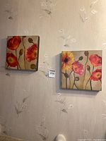 Shows two 12x12 inch canvas prints of floral artwork mounted on a wallpapered wall, featuring red and yellow poppies with green stems.