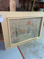 Framed watercolor painting resting on floor showing overall artwork and cream wooden frame.