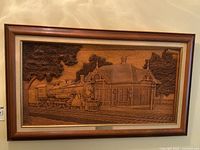 Full view of framed wood carving showing train and building scene