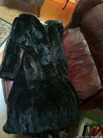 Full length black mink fur coat laid on brown leather chair, showing the shiny mink fur.