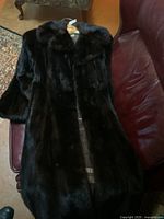 Photo of full length black mink fur coat laid on a red leather surface, showing overall length and condition.