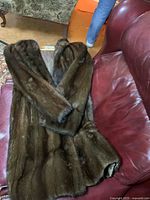 Full view of the full length mink fur coat laid over a red leather sofa.