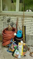 Photo of stacked terracotta-colored garden edging, wicker basket, metal trellis, bamboo stakes, watering can, and bags of potting soil and mulch outside on concrete
