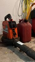 Orange Husqvarna 132 HBV gas leaf blower next to red gas can, showing nozzle damage.