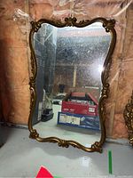 Front view of an ornate gilded framed mirror showing the overall design and reflection of basement surroundings