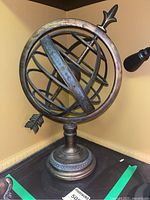 Front angle of metal armillary globe on ornate base showing engraved rings and arrow design.