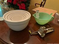 Photo showing set of five white nesting bowls, green Fire King pitcher, and metal rotary cheese grater on dining table.
