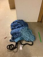Blue nylon hammock crumpled on concrete floor with black nylon strap and loops visible.