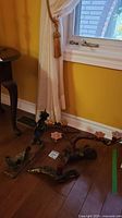 Photo of two handcarved wooden candelabras and a wood sea dragon sculpture placed on the floor near a window with yellow walls and a brown wooden floor