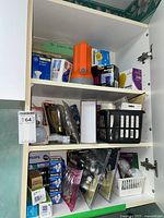Full view of cabinet shelves containing an orange flashlight, boxed GE Indoor floodlight bulbs, decorative light bulbs, Philips light bulbs, halogen bulbs, and other assorted lighting supplies.
