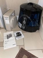 Homedics humidifier and Philips fan heater placed next to each other on tiled floor with instruction manuals.