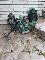 Group photo showing all four iron decorative items on an outdoor brick surface: owl lantern, black lantern, planter with ivy, and two-ring candle holder stand.