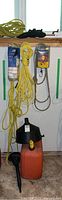 Photo showing orange 22L jerry can with black spout, yellow nylon rope, white rope in packaging, and yellow funnel in packaging hanging on wall.