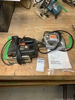 Wide view of two jigsaws on a wooden surface along with instruction manual and power cords visible