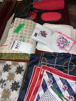Image showing an assortment of linen and lace doilies, embroidered kerchiefs, travel pouches, and fabric pieces with varied patterns and colors.