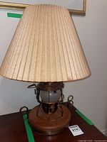 Full view of the copper lantern table lamp with beige pleated shade on wooden base.