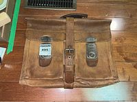 Front view of the vintage brown leather briefcase showing two buckle clasps and central securing strap with handle on top.